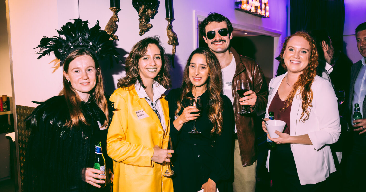 Party attendees in eclectic costumes, including vintage and whimsical themes, share a toast.