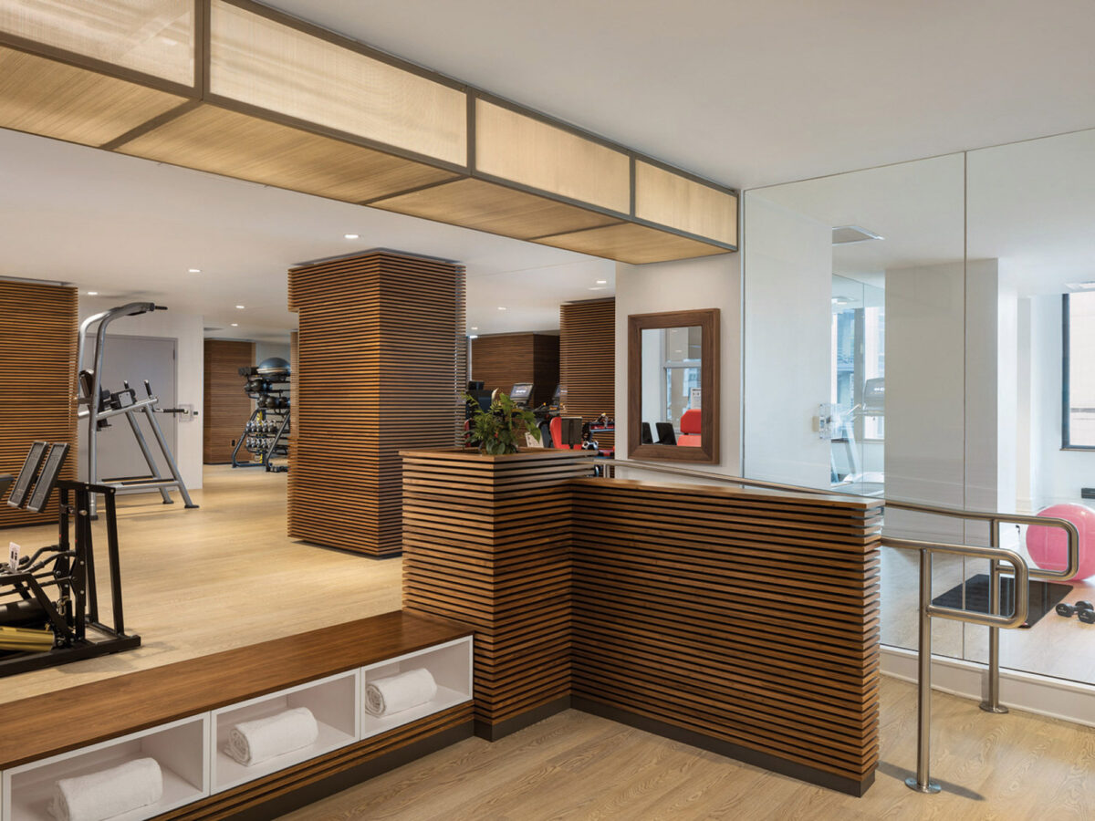 Modern home gym with natural light, featuring wooden slat partitions for privacy, white walls, reflective mirrors, and a variety of fitness equipment. Integrated storage keeps the space organized and inviting.