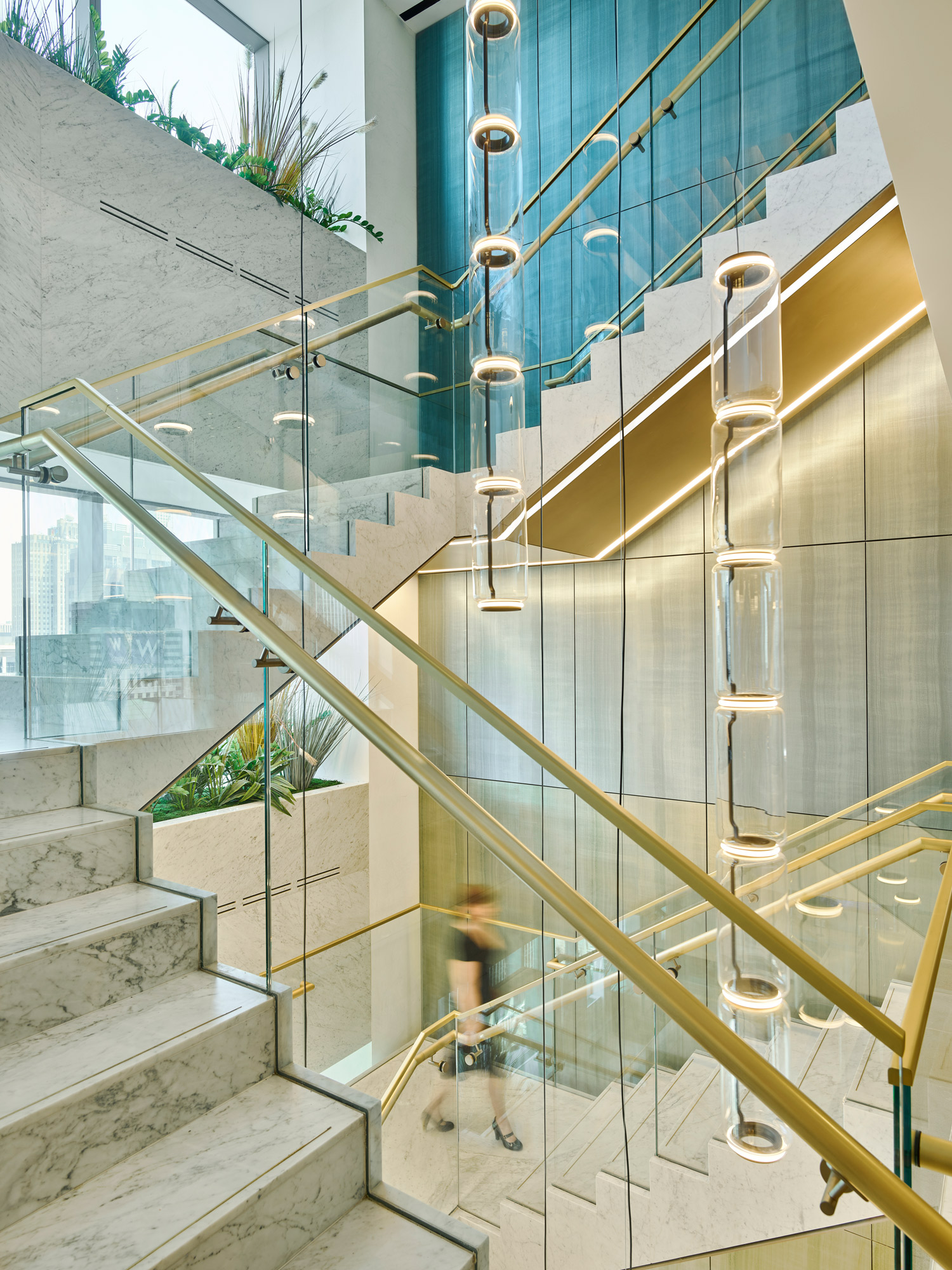 A modern staircase in a corporate building with vertical light fixtures, glass balustrades, and a person descending.