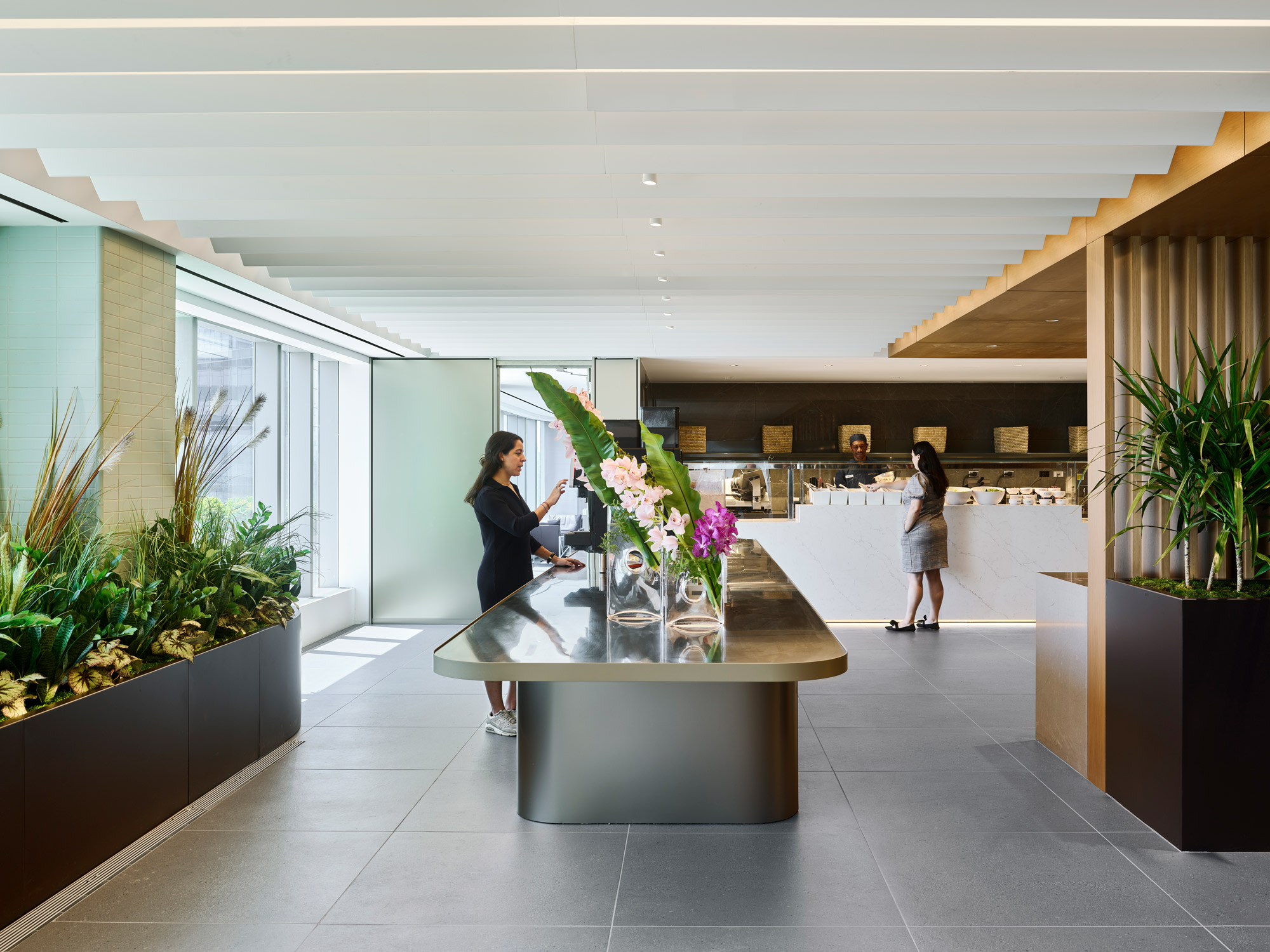 A reception area in a modern office featuring a sculptural desk, ample greenery, and natural lighting.