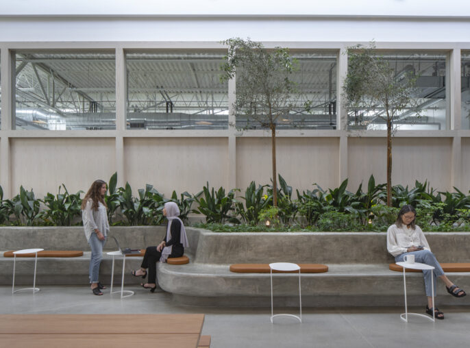 Spacious lobby with a biophilic design featuring an indoor garden bed, wooden paneling, and a skylight. Modern benches and side tables accommodate visitors amid the lush greenery, combining functionality with a connection to nature.