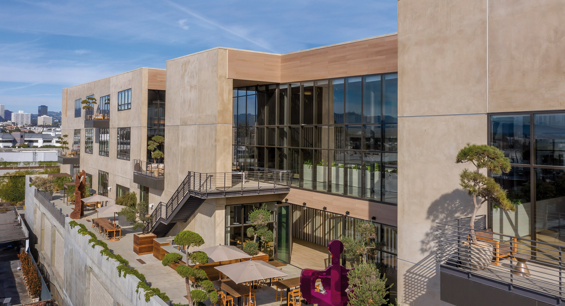 Modern urban building with a rooftop garden and outdoor seating area, showcasing sustainable architecture in a cityscape.