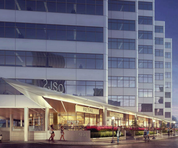 Contemporary glass building facade at dusk, featuring staggered rectilinear forms, reflective windows, and integrated retail space beneath an illuminated angled marquee.