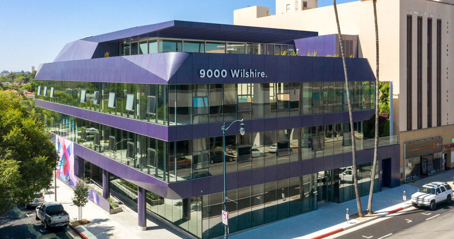 Modern commercial building on Wilshire Boulevard with a distinctive purple facade and geometric design, featuring large windows, and an angular structure that offers a dynamic urban presence.