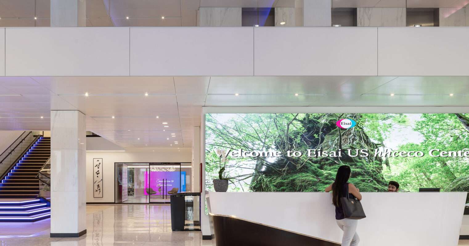 Modern corporate lobby featuring a sleek, white reception desk with embedded LED lighting. A large digital display showcasing nature imagery provides a vibrant backdrop, enhanced by the juxtaposition of minimalist staircases and clean, reflective flooring.