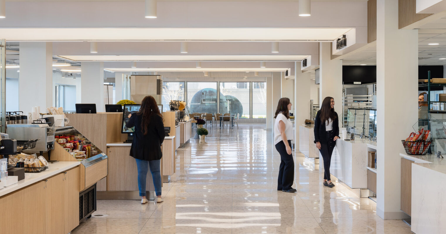 Spacious cafe interior featuring polished marble flooring, modern recessed lighting, and a sleek, minimalist serving area with glass display cases. Patrons converse casually, enhancing the inviting ambiance.