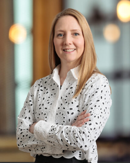 The image features a person wearing a detailed white blouse, standing in a well-lit indoor setting.