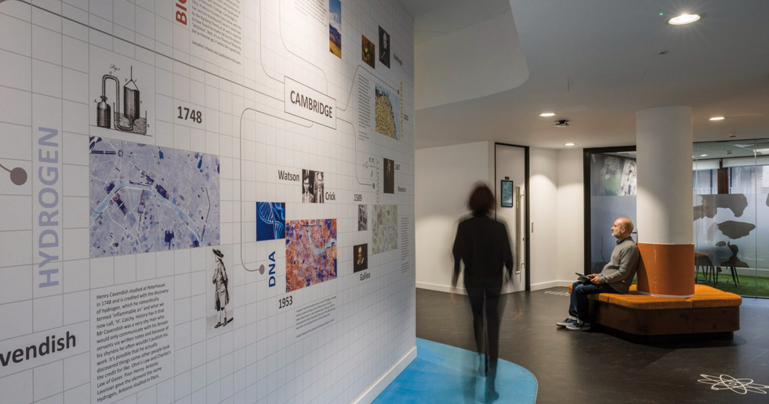 Modern office lobby with interactive wall exhibit featuring a timeline of scientific achievements, comfortable seating area, and soft ambient lighting enhancing the space's innovative atmosphere.