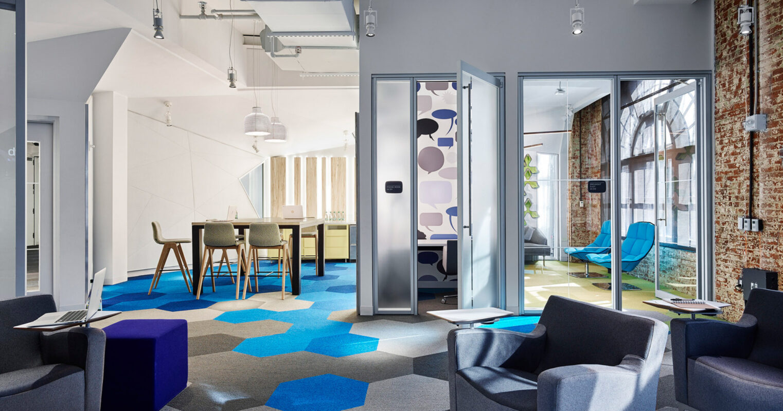 Modern office space blending industrial and contemporary design, featuring exposed brick walls, geometric carpet patterns, sleek furniture, glass partitions, and an eclectic mix of blue and neutral tones for a dynamic work environment.