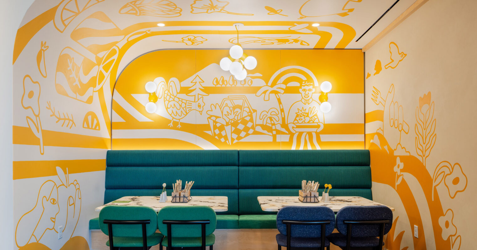 Vibrant dining area featuring a whimsical, large-scale mural with abstract shapes and figures in goldenrod and white. Teal banquet seating and dark blue chairs complement the artwork, while white globular pendant lights add a modern touch to the space.