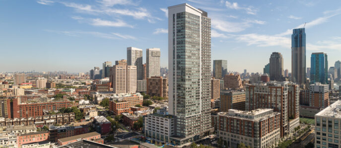Modern urban landscape showcasing a mix of architectural styles with a prominent glass facade skyscraper, reflecting the cityscape under a clear blue sky.