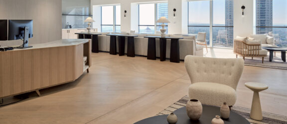 Modern interior featuring an open-plan kitchen with sleek, curved island and bar stools, accentuated by wooden flooring and minimalist decor. Natural light floods the space, highlighting clean lines and a neutral color palette.