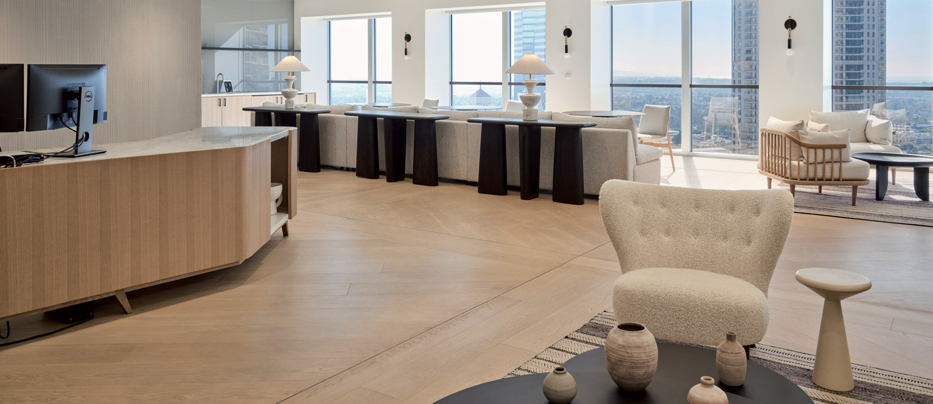 Modern interior featuring an open-plan kitchen with sleek, curved island and bar stools, accentuated by wooden flooring and minimalist decor. Natural light floods the space, highlighting clean lines and a neutral color palette.