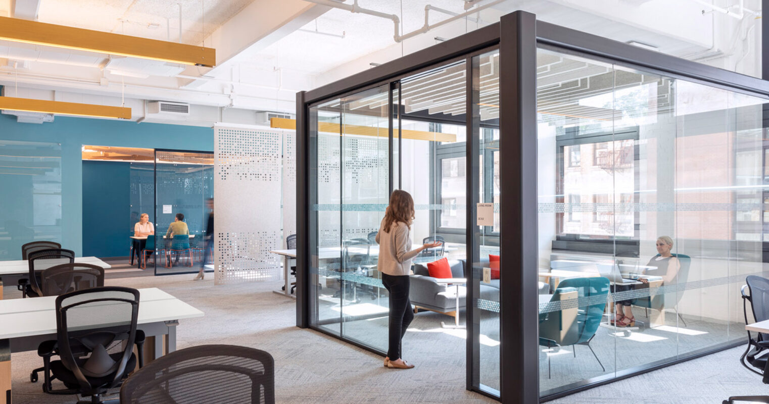 Modern open-plan office space featuring clear glass partitions, sleek black frames, and vibrant yellow accent walls. Natural light floods the area, highlighting the eclectic mix of collaborative workstations and private meeting rooms.