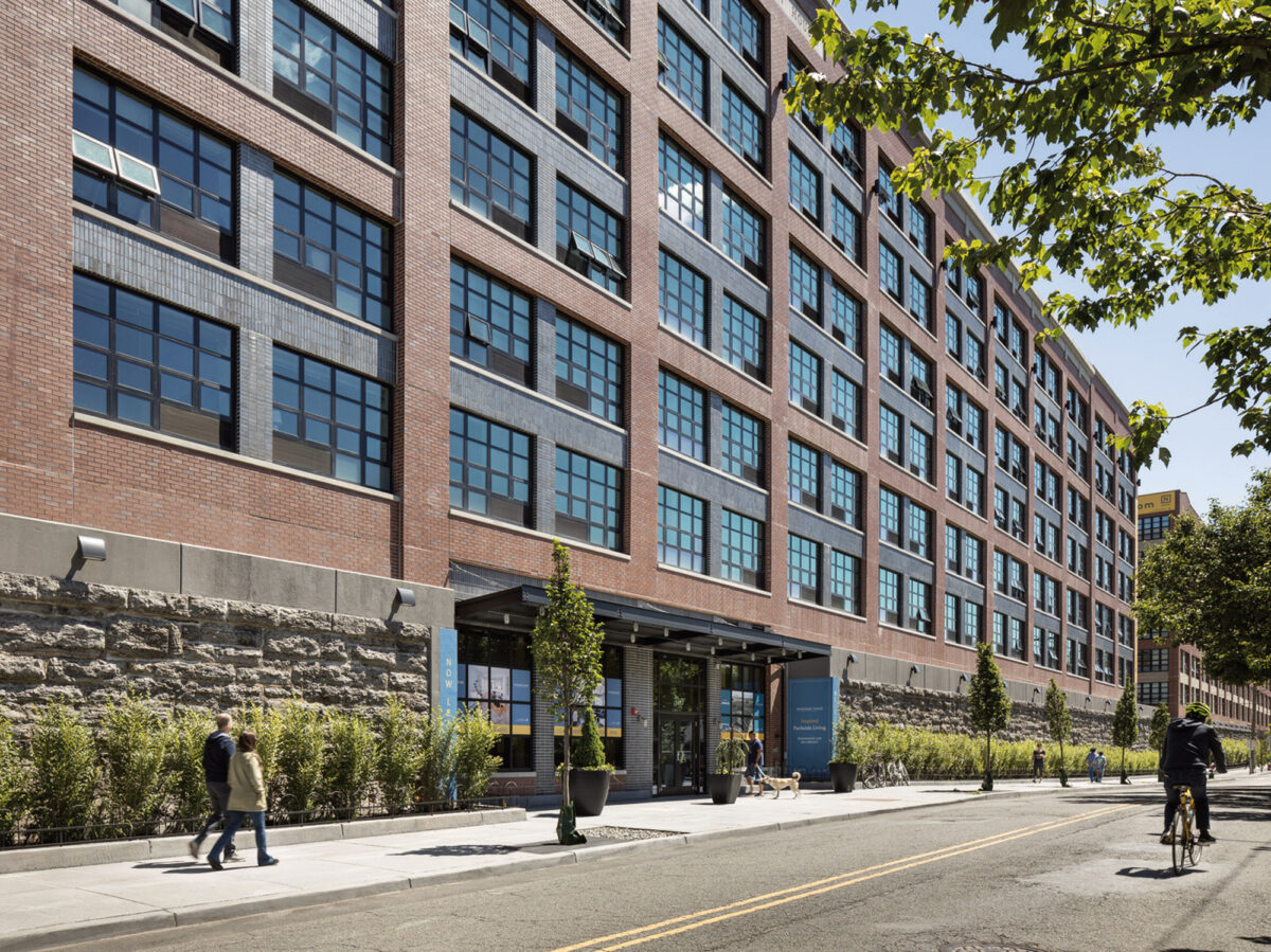 Elegant urban building facade with expansive windows, featuring balanced symmetry, warm brickwork, and a contemporary entrance flanked by greenery and welcoming planters.