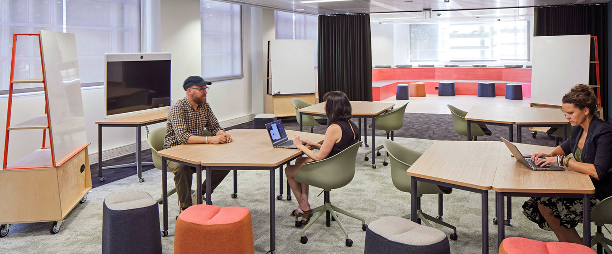 Modern office workspace featuring a neutral color palette with accentuated pops of orange and red. Collaborative layout includes mobile partition boards, ergonomic seating, and versatile workstations for dynamic use and productivity.