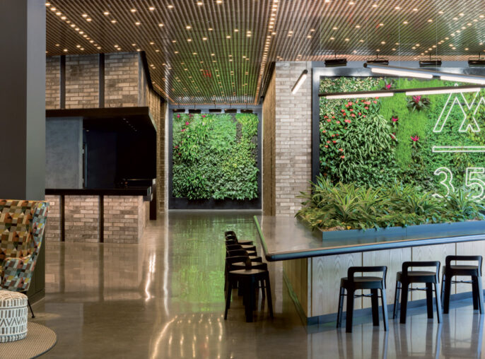 Contemporary lounge area boasting an illuminated pegboard ceiling and glossy floor, with a green living wall featuring numerical art, flanked by industrial-style seating and vibrant planters.