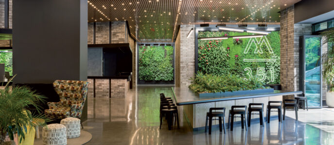 Contemporary lounge area boasting an illuminated pegboard ceiling and glossy floor, with a green living wall featuring numerical art, flanked by industrial-style seating and vibrant planters.