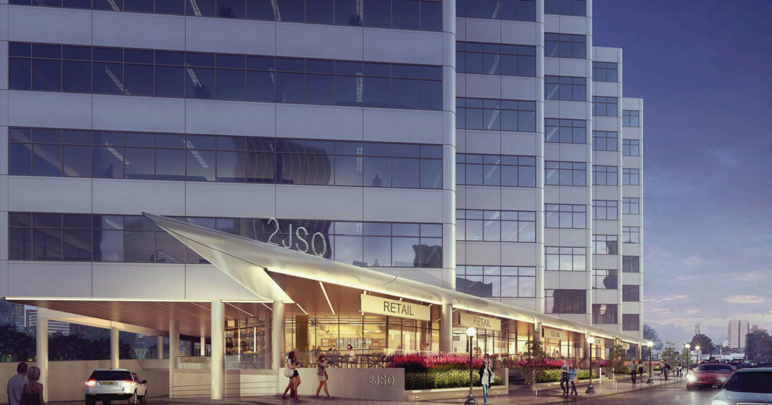 Contemporary glass building facade at dusk, featuring staggered rectilinear forms, reflective windows, and integrated retail space beneath an illuminated angled marquee.