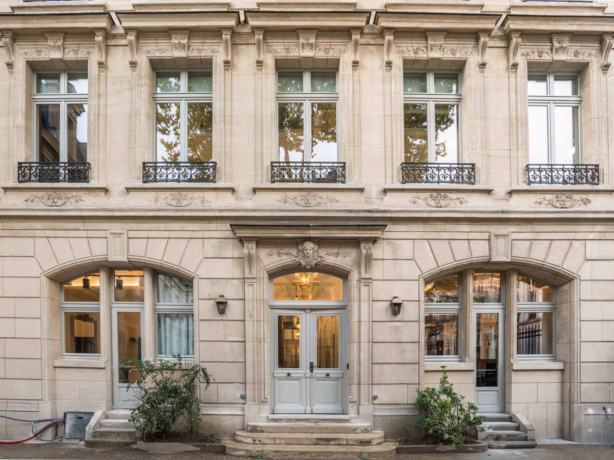 Classic French Beaux-Arts architecture features prominently with intricate stone facades, symmetrically balanced French windows, and wrought-iron balcony detailing flanking a central wooden door with transom window.
