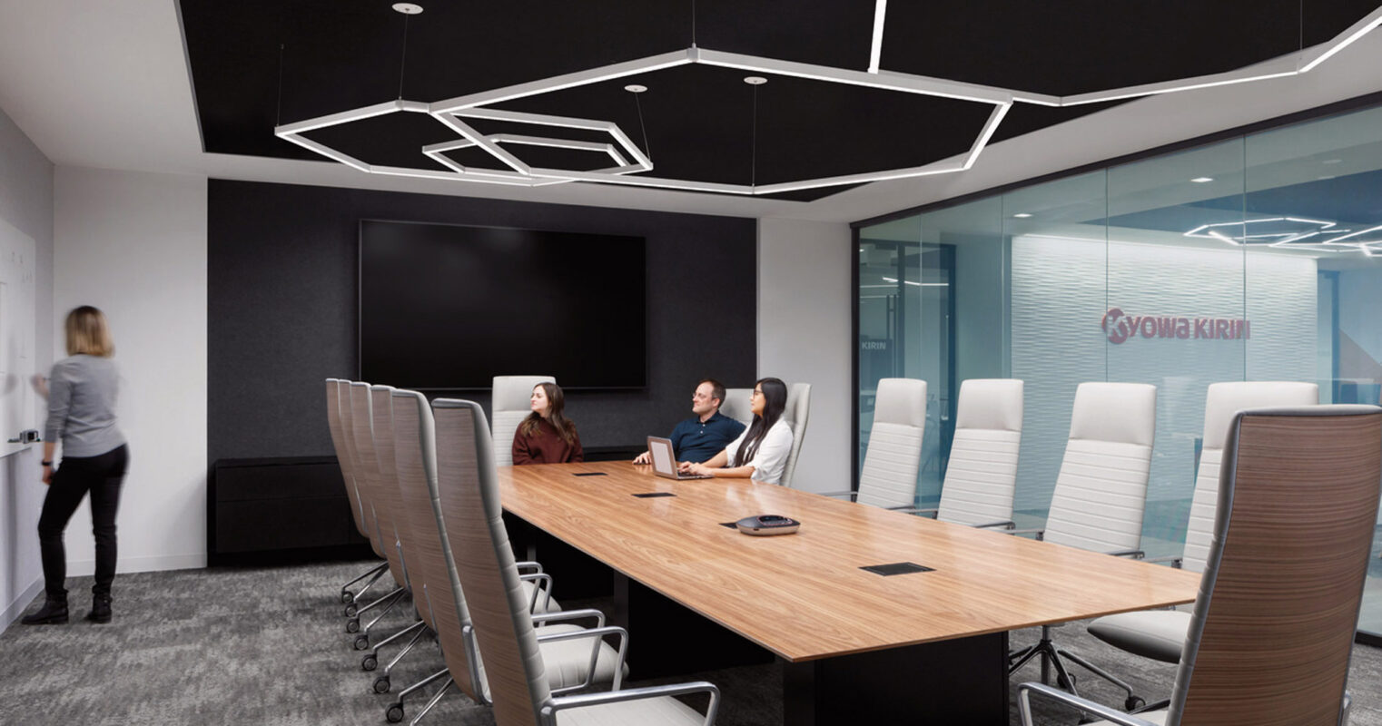 Contemporary boardroom featuring an elongated wooden table with surrounding mesh-back chairs, angular overhead lighting elements, and glass walls providing a glimpse into the adjacent office.
