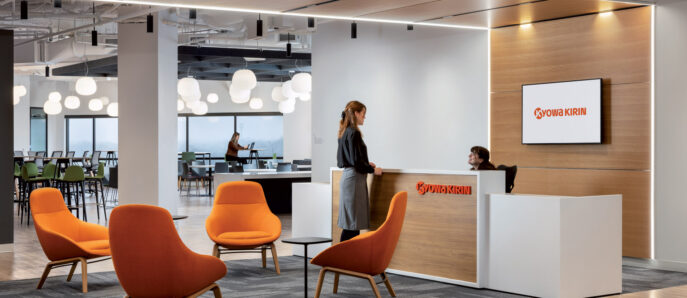 Modern office lobby featuring a sleek reception desk with a lit company sign, vibrant orange chairs adding a pop of color, and pendant lighting illuminating the open, airy space.