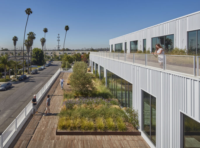 Modern office building integrating green spaces: an employee enjoys a lush rooftop garden walkway, with palm trees and blue skies in the background, emphasizing eco-friendly design and work-life balance.