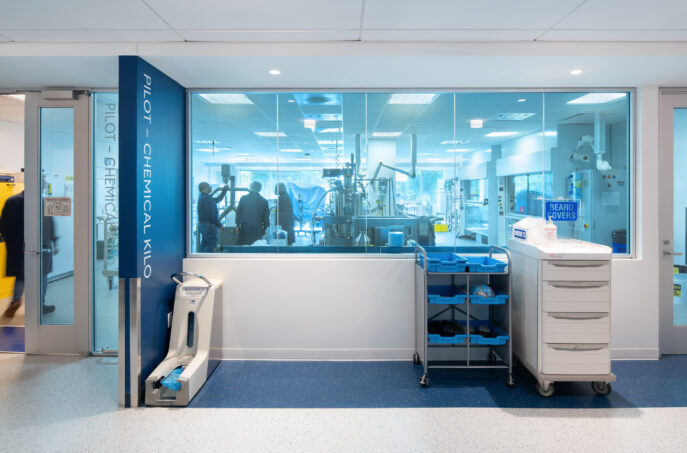 Modern laboratory interior featuring a bright, open design with large glass windows. The space showcases advanced equipment and a streamlined layout, emphasizing functionality and collaboration. A mobile cart with storage bins stands in the foreground, alongside modern lighting that enhances the sterile atmosphere.