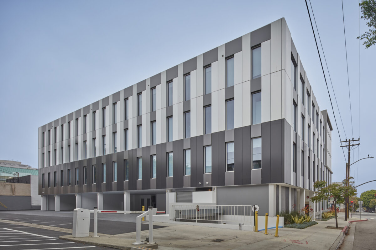 Modern commercial building featuring a striking façade of alternating black and white panels, which creates a dynamic visual rhythm. Large, vertically aligned windows enhance natural light while complementing the sleek lines of the structure. The minimalist design is further emphasized by a subtle entrance and landscaped surroundings.