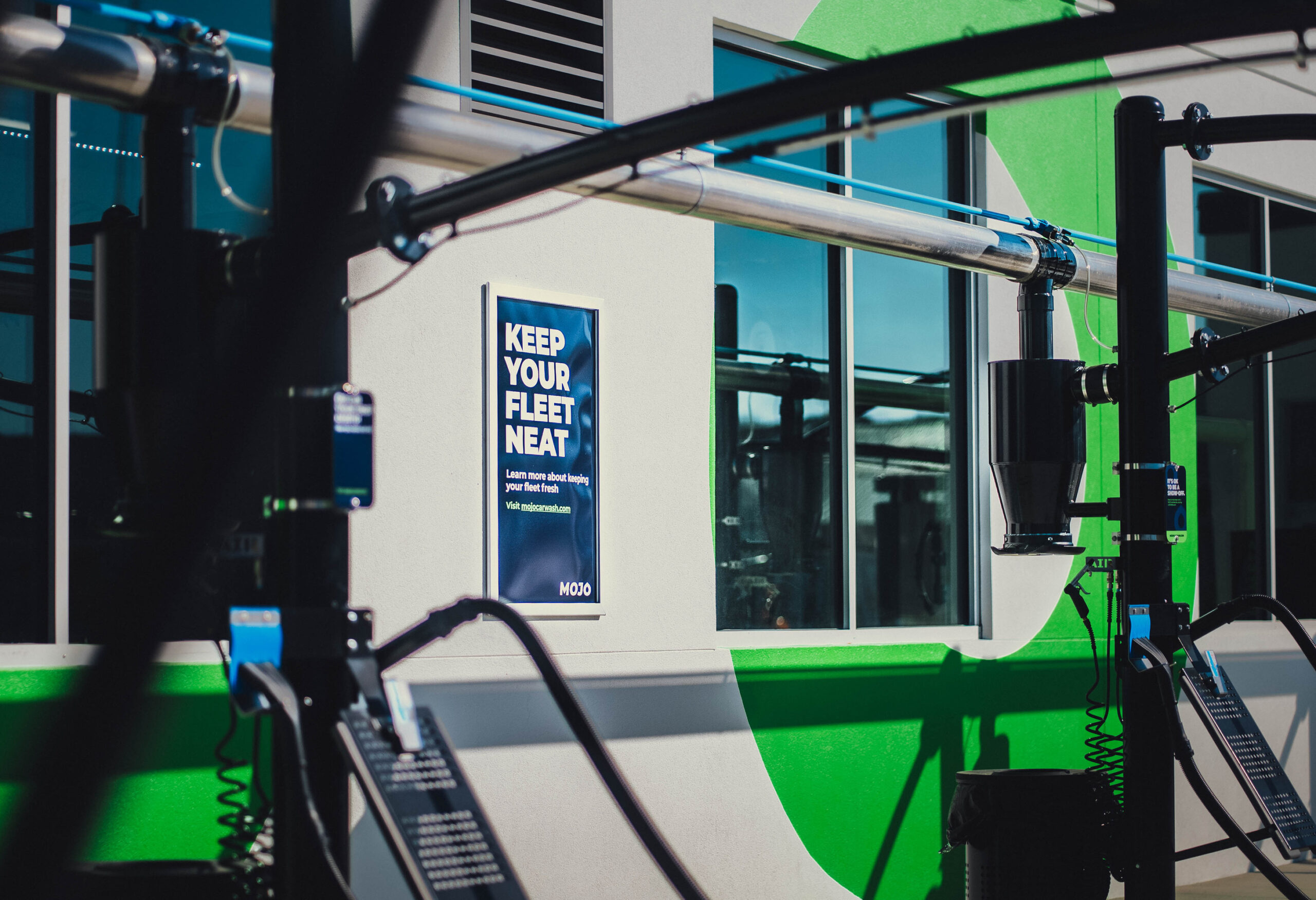 Bright green accents contrast against a clean, white wall, enhancing the modern aesthetic. A prominent blue sign with bold typography communicates a message about maintenance, while sleek, industrial equipment occupies the foreground, emphasizing functionality and design sophistication in a commercial environment. Natural light filters through large windows, highlighting the space's openness.