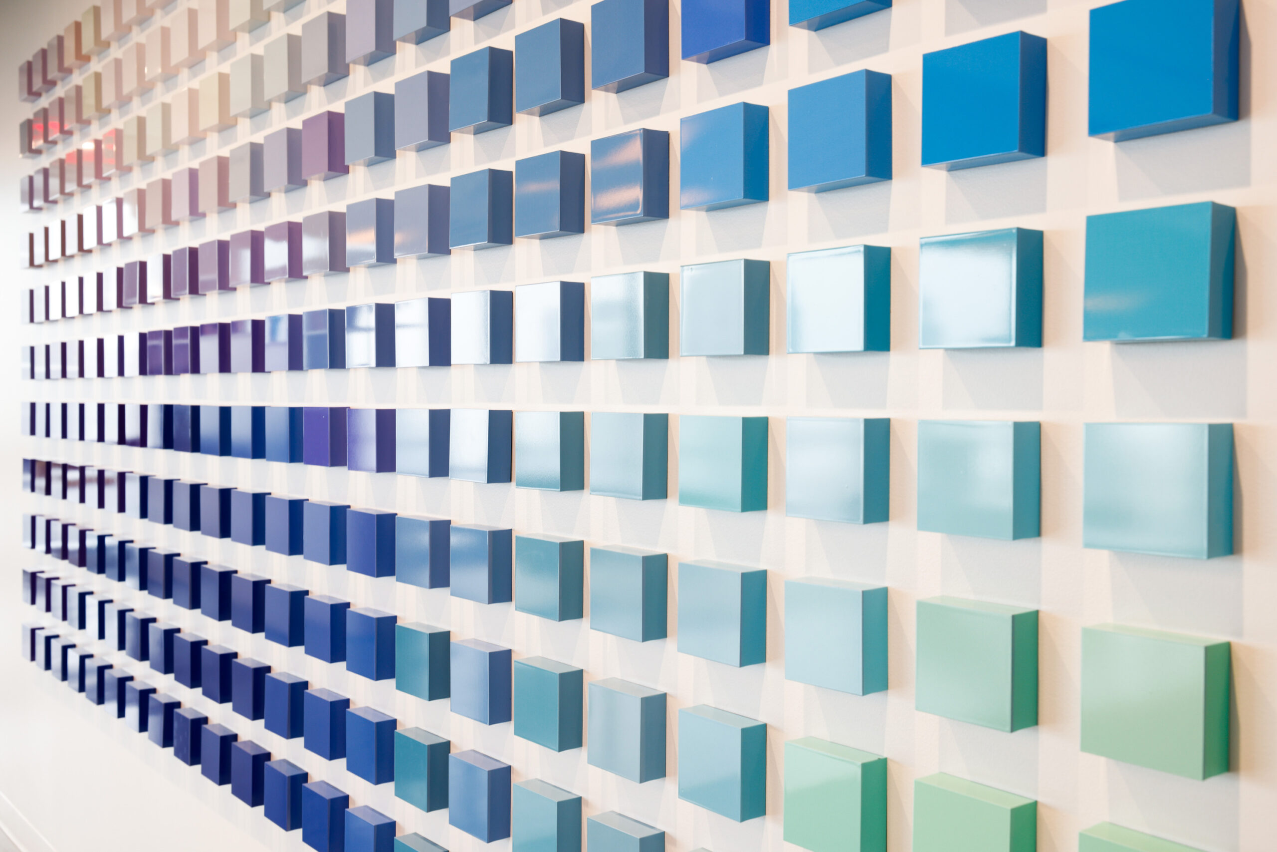 A visually striking wall displays a gradient of colorful paint swatches arranged in neat rows. The swatches transition smoothly from deep blues to soft greens, showcasing a variety of finishes. This design element highlights the importance of color selection in creating harmonious interior spaces.
