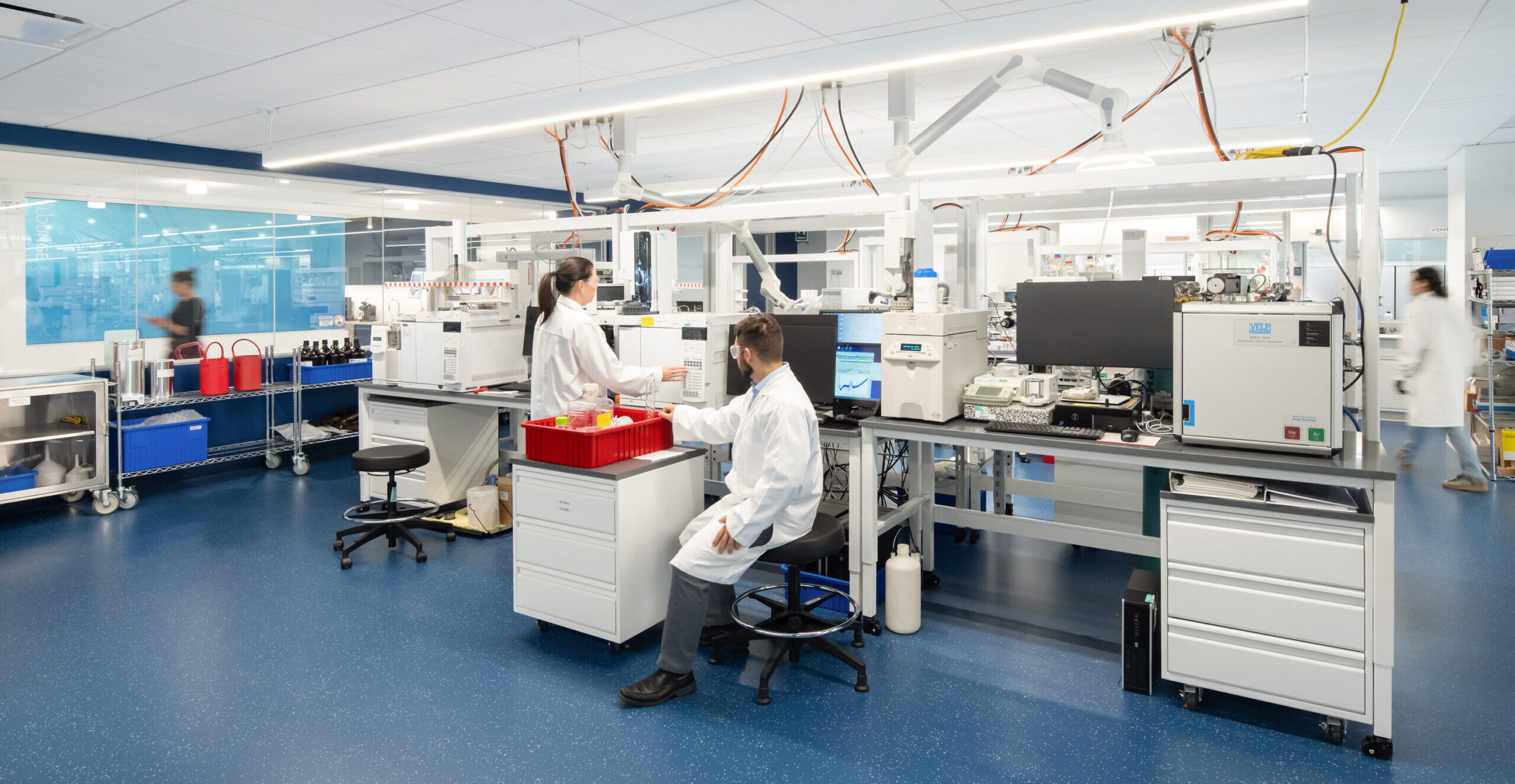 Modern laboratory environment featuring sleek, modular workstations equipped with advanced scientific equipment. The spacious layout promotes efficiency and collaboration among staff members, dressed in lab coats, as they engage in research activities. Bright lighting highlights the clean lines and functionality of the design, enhancing productivity in a professional setting.