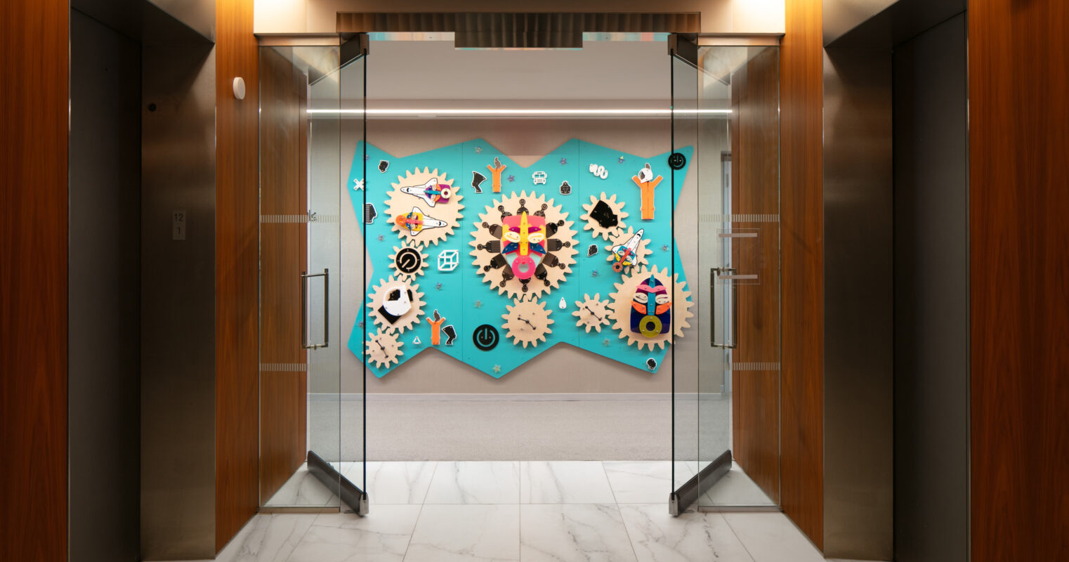 Brightly colored wall art featuring whimsical gears and playful icons dominates the central space between two modern glass doors. The backdrop is a vibrant turquoise, contrasting with the sleek wood paneling and polished marble floor, creating an engaging and creative entryway that invites interaction.
