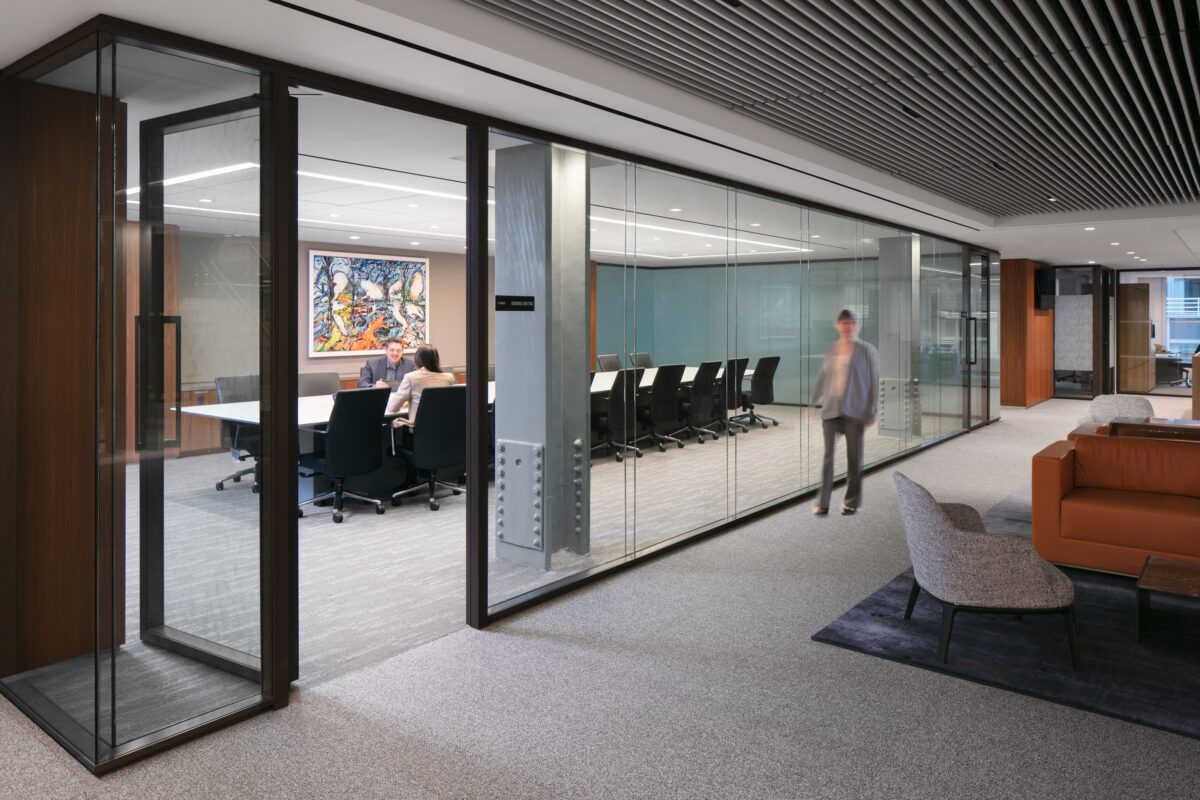 Modern office interior featuring a transparent glass conference room, enhancing visibility and collaboration. The space showcases sleek design elements, including a comfortable seating area with contemporary furniture. The rich color palette encompasses earthy tones, complemented by vibrant artwork, fostering a creative, inviting atmosphere conducive to productivity.