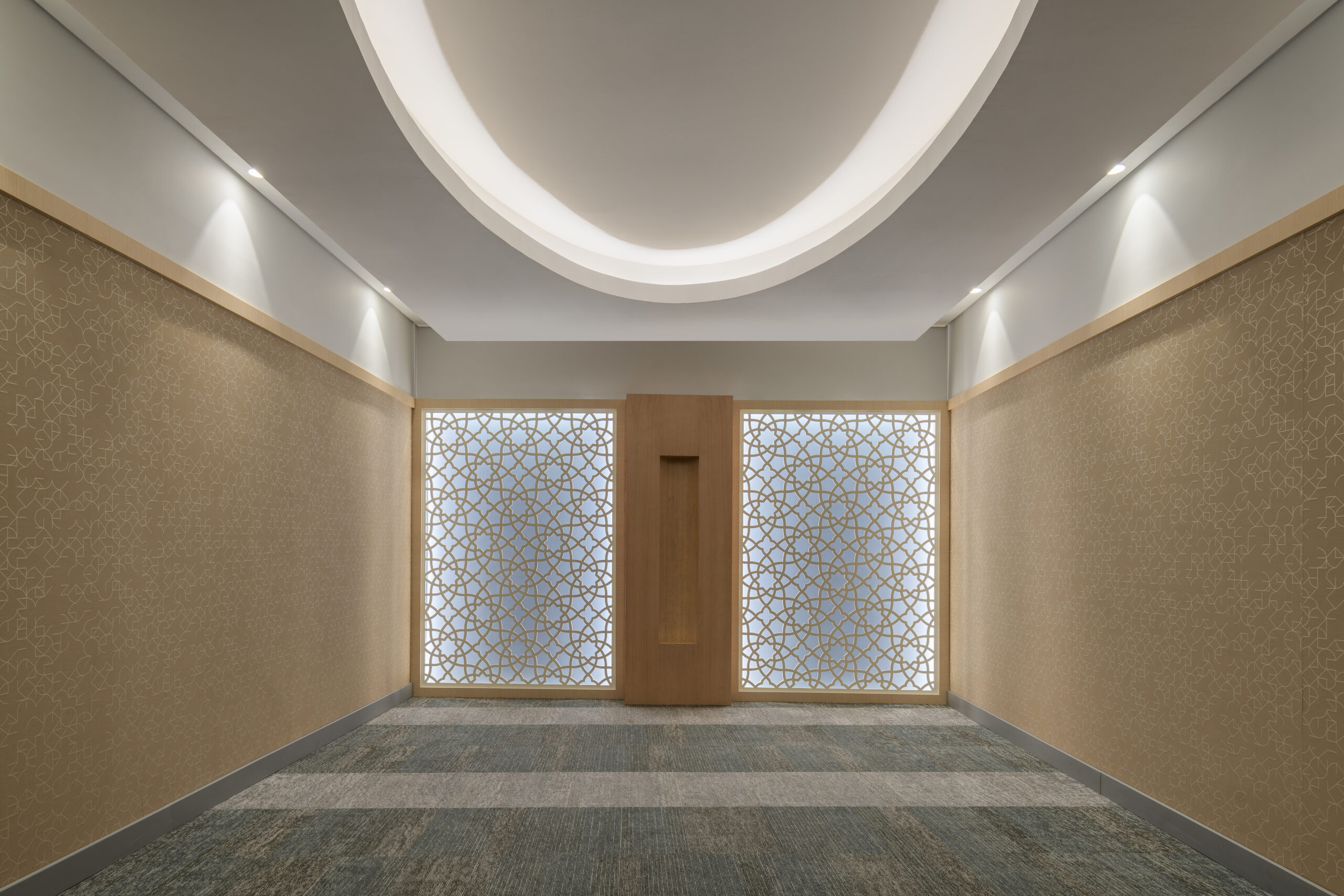 Elegant corridor featuring textured wallpaper with intricate patterns, complemented by an arched ceiling illuminated by recessed lighting. Decorative lattice screens on both sides provide privacy while enhancing visual appeal. The muted color palette and soft carpeting create a serene atmosphere, ideal for a contemporary interior space.