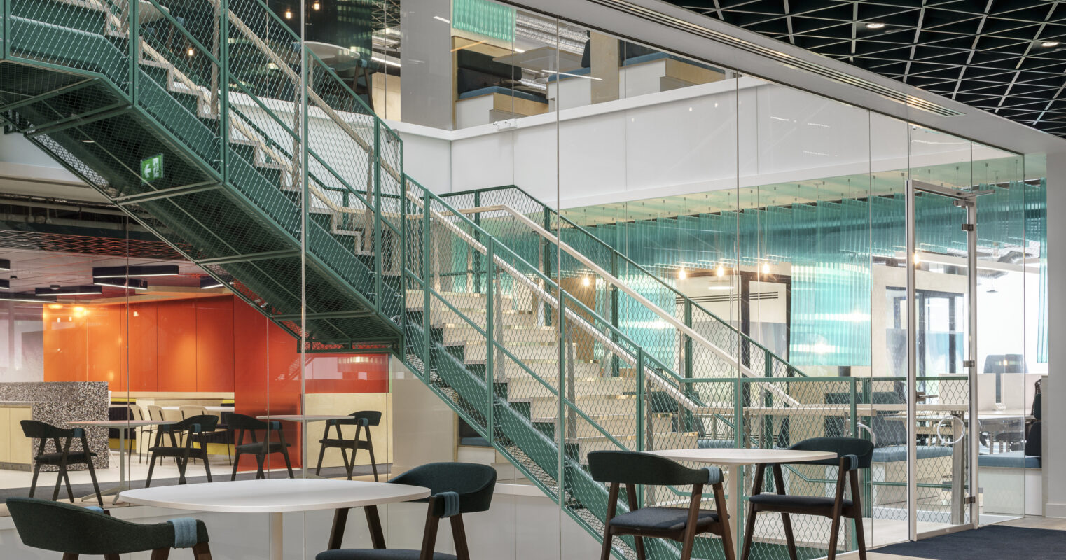 A modern office interior showcases a dynamic open space with a striking staircase featuring green metal mesh railings. Glass partitions enhance transparency, while minimalist furniture in a neutral palette adds elegance. Vibrant hues in the background and geometric ceiling design create an inviting atmosphere for collaboration and creativity.