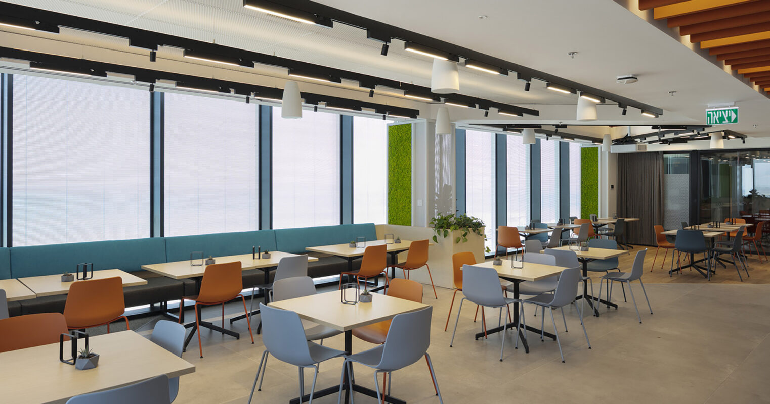 Modern dining area featuring sleek, minimalist furniture in muted tones. Natural light floods through large windows, complemented by greenery on the walls. The layout includes a mix of chairs and tables, promoting a casual yet contemporary atmosphere for dining and collaboration. Stylish lighting fixtures enhance the space's ambiance.