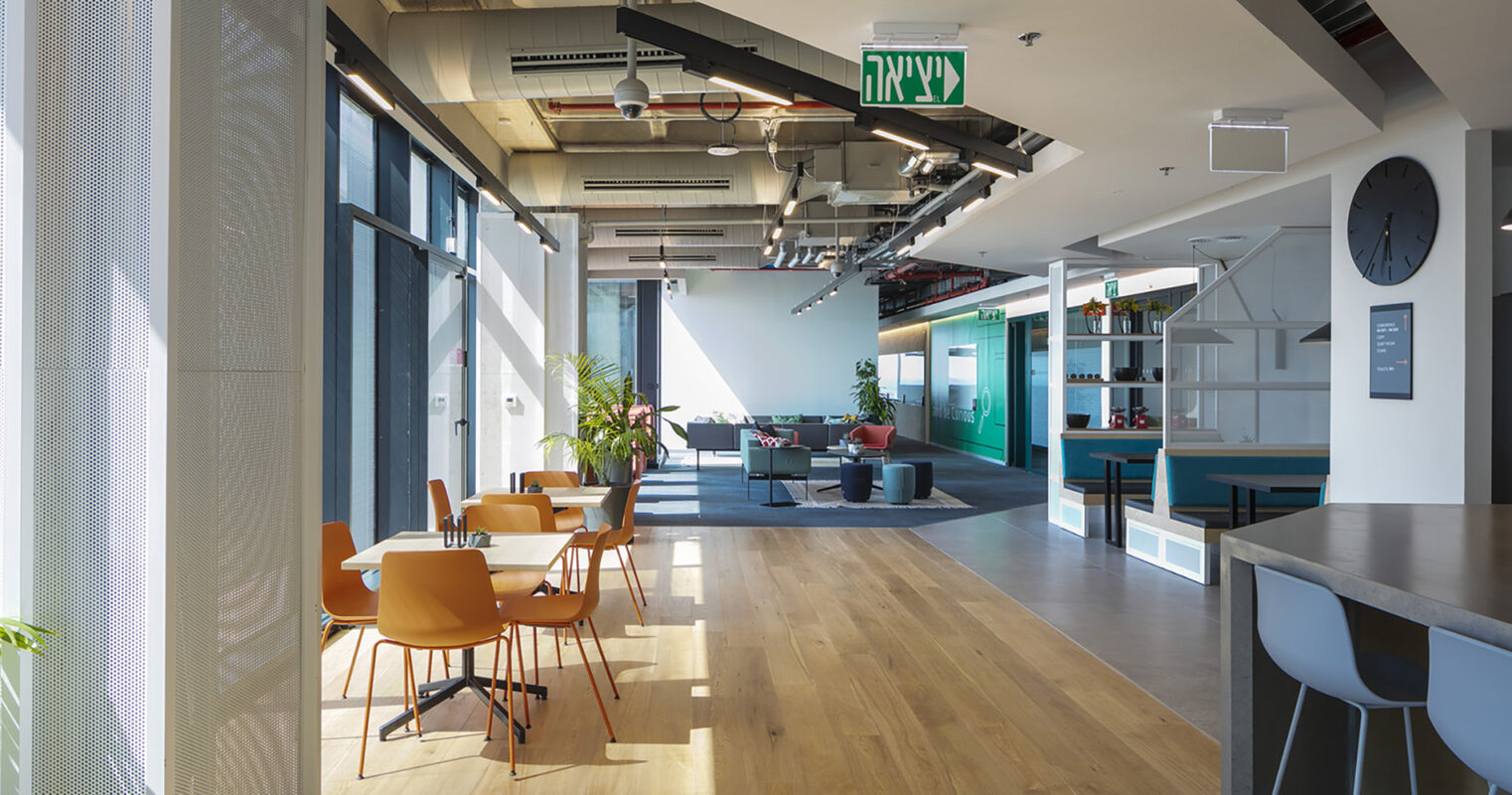 Natural light floods this modern open-plan office, showcasing polished wooden flooring and contemporary furnishings. Stylish orange chairs surround sleek white tables, while spacious lounge areas feature vibrant green accents and cozy seating. Architectural elements, such as exposed ductwork and minimalist design, enhance the innovative atmosphere, promoting collaboration and creativity.