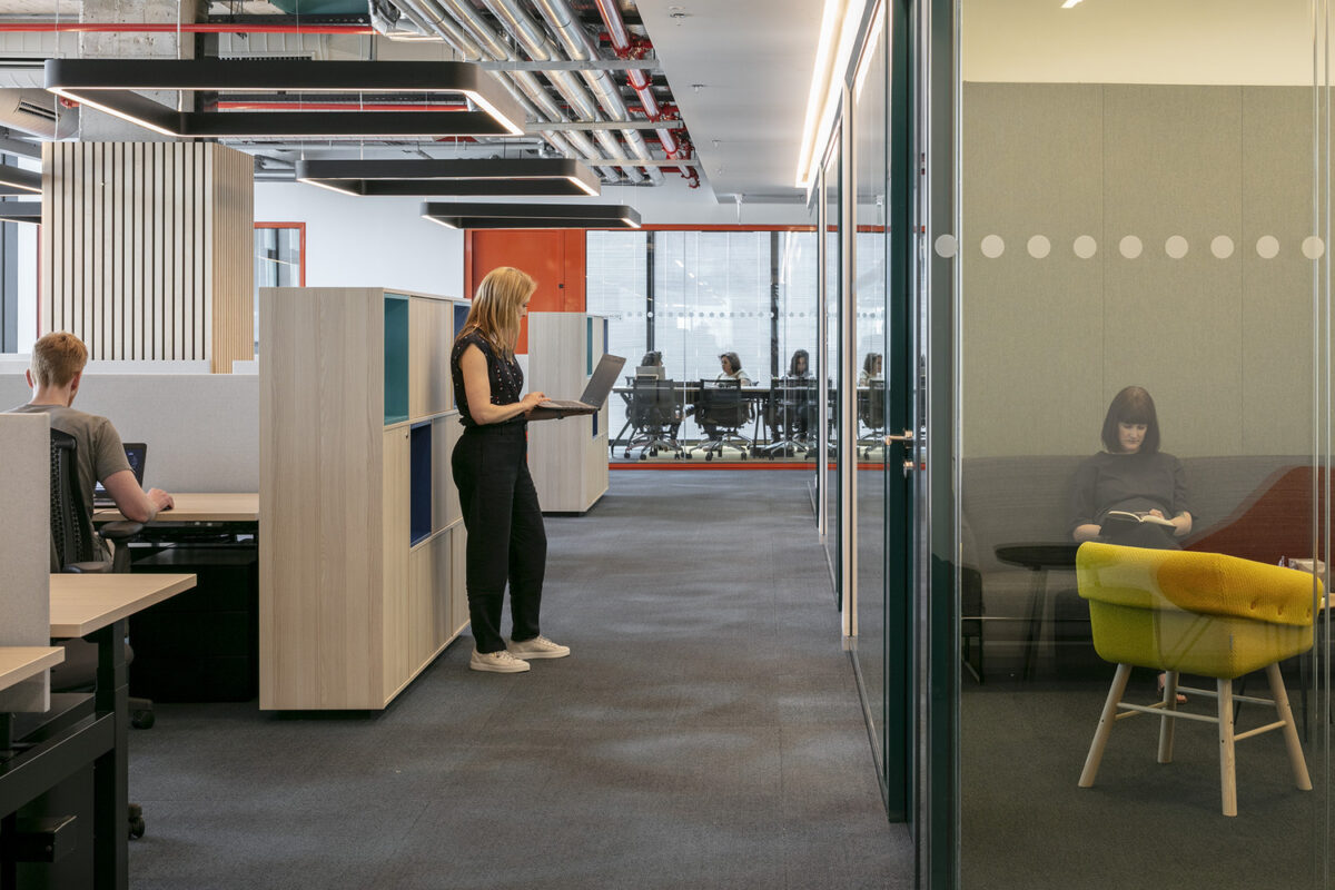 Open office layout featuring modular workstations and private meeting areas. Brightly colored accents complement the minimalist design, while glass partitions enhance transparency and collaboration. A comfortable lounge area with vibrant seating invites relaxation amidst the modern workspace, promoting creativity and productivity among employees.