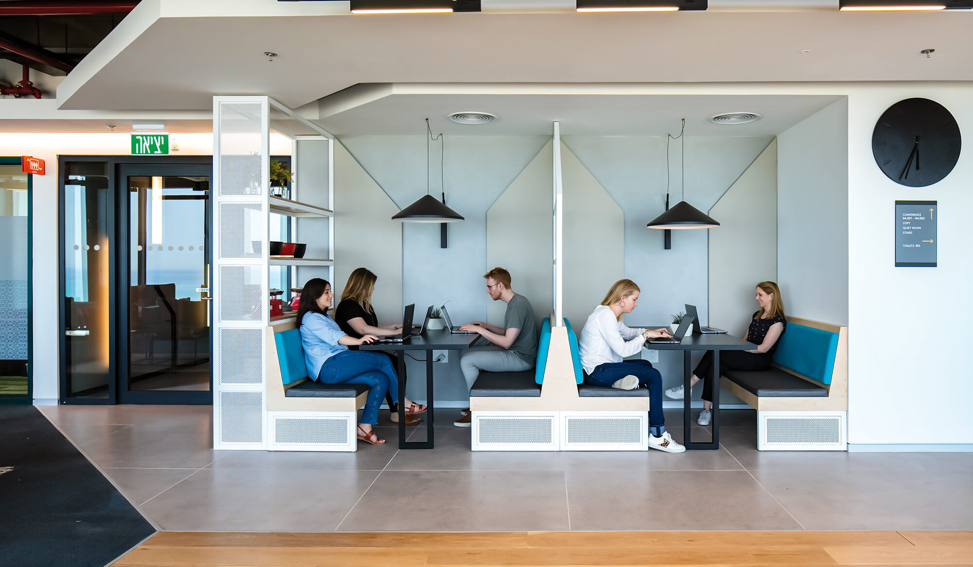 Modern co-working space featuring a combination of shared seating and private pods. Light-colored walls contrast with vibrant blue upholstery, promoting productivity and collaboration. Oversized pendant lights provide focused illumination, while large windows ensure ample natural light, enhancing the inviting atmosphere for professionals and creatives.
