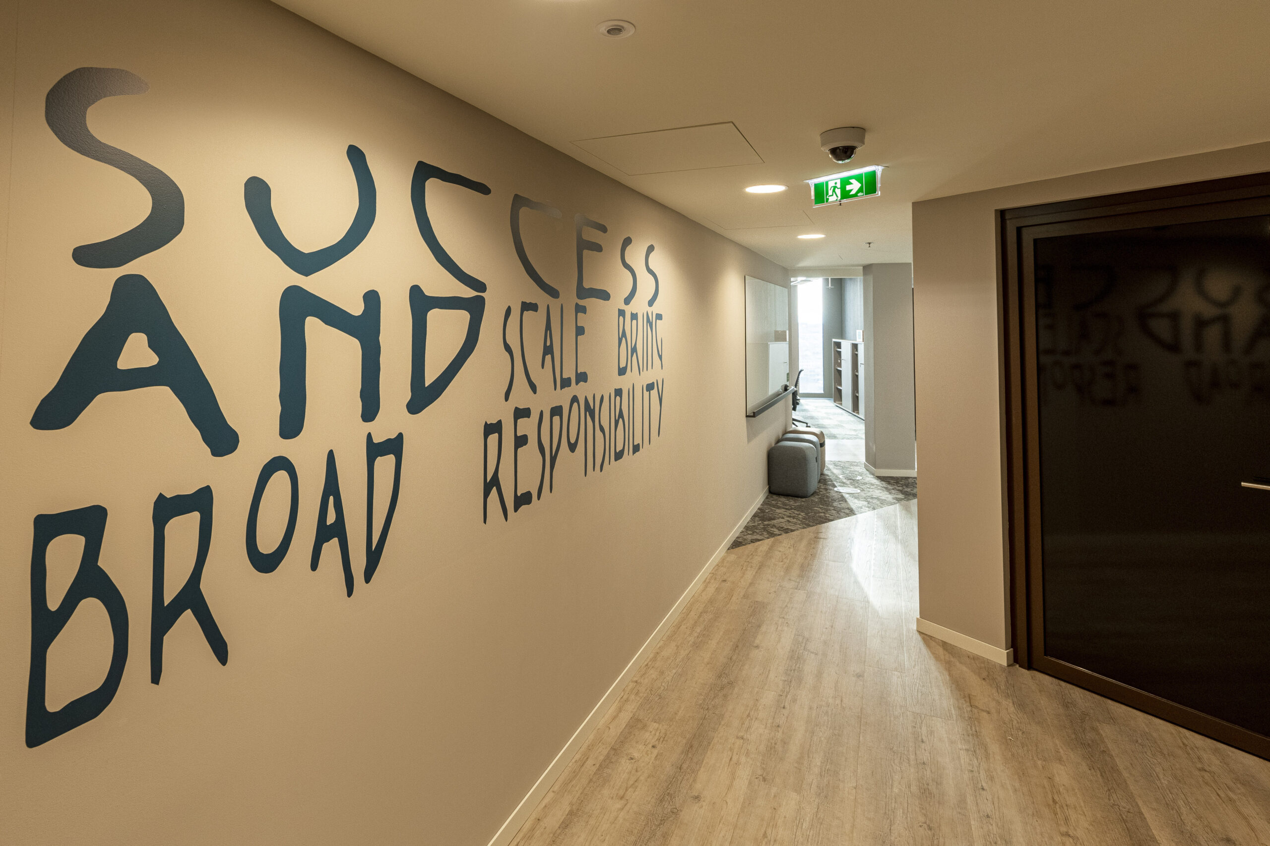 A contemporary hallway featuring a large, bold typographic mural that emphasizes key concepts such as "Success," "Broad," and "Responsibility." The neutral-toned walls contrast with the creative typography, while sleek flooring and minimalist furniture enhance the modern atmosphere, reflecting a focus on both aesthetics and functionality in interior design.