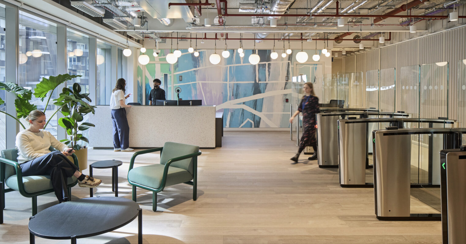 Contemporary office lobby featuring a minimalist reception desk with a textured surface. Soft seating areas offer green accent chairs and low tables, surrounded by large windows allowing natural light. A backdrop of abstract wall art adds visual interest, while indoor plants contribute to a welcoming atmosphere.