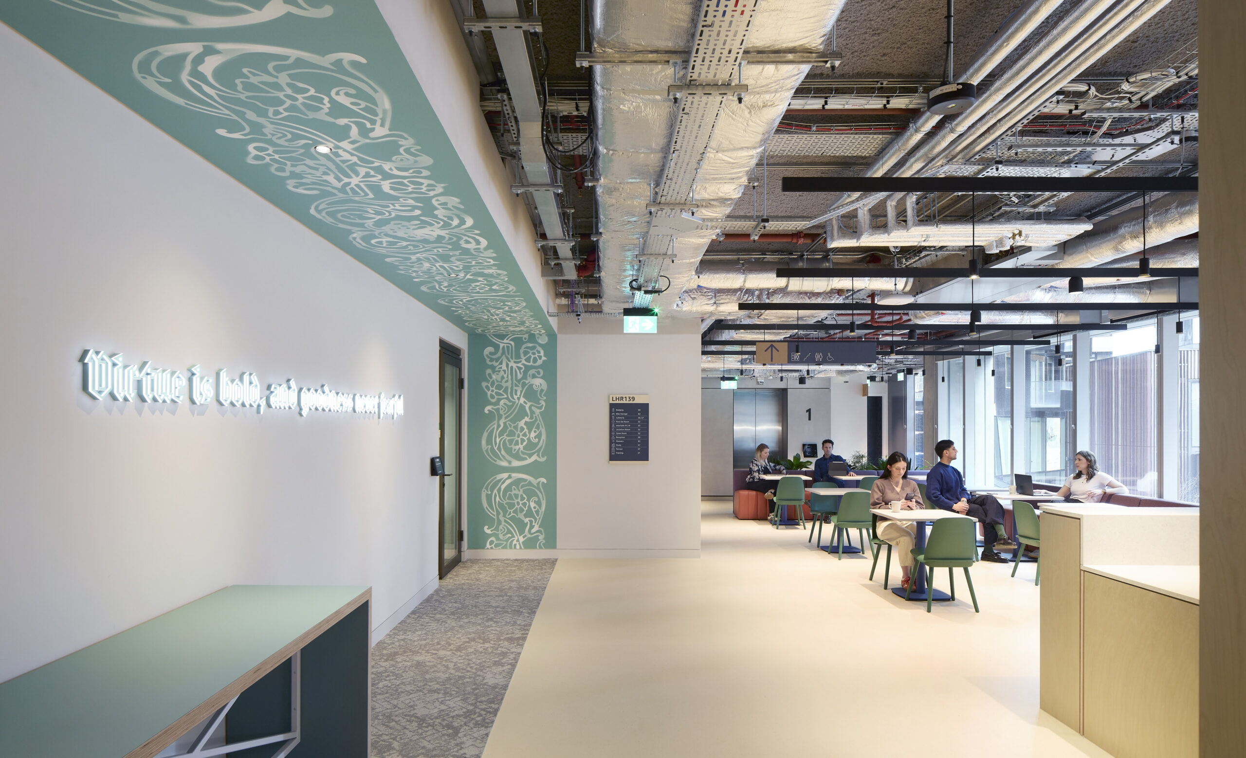 A modern office interior featuring open workspaces and collaborative areas. Exposed ceiling elements enhance the industrial aesthetic, while green accents and contemporary furnishings provide a fresh, inviting atmosphere. Wall art with inspiring text adds a creative touch, encouraging productivity and collaboration among employees.