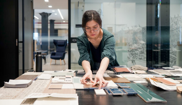 Interior designer is curating material samples, textured finishes, and a neutral color palette under bright architectural lighting for a contemporary commercial interior design project in a modern design studio.