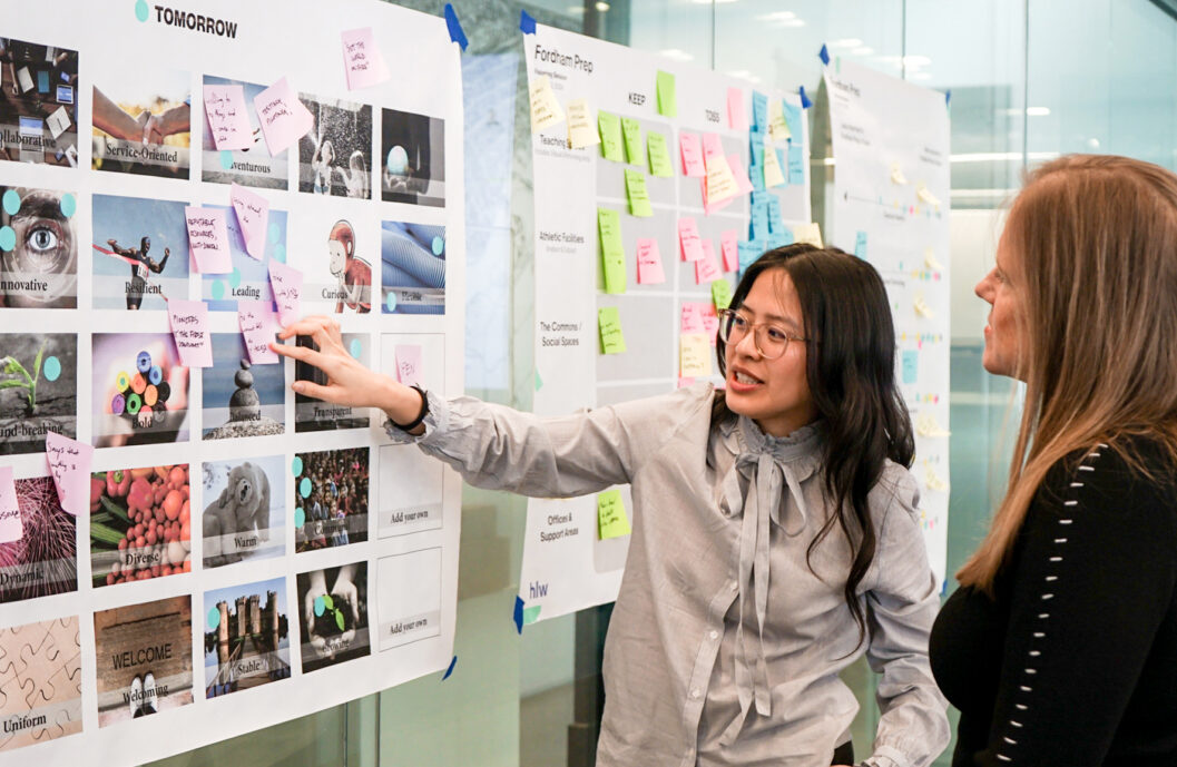 Team members participate in a collaborative visioning workshop, reviewing inspiration boards and stakeholder feedback on a wall display within a modern workplace design studio for workplace design.
