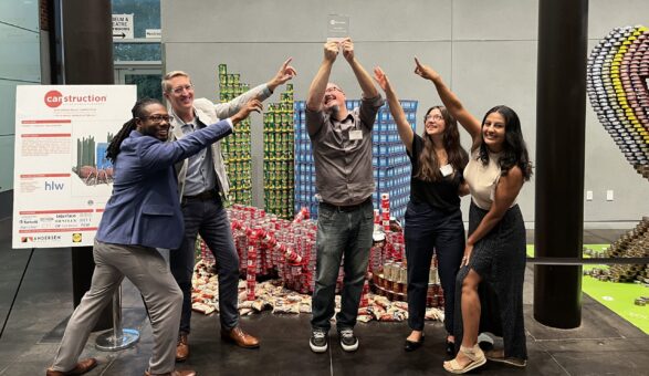 HLW team members pose beside a Canstruction installation built from stacked food cans, showcasing community engagement, creative problem-solving, and philanthropic participation within the design industry.
